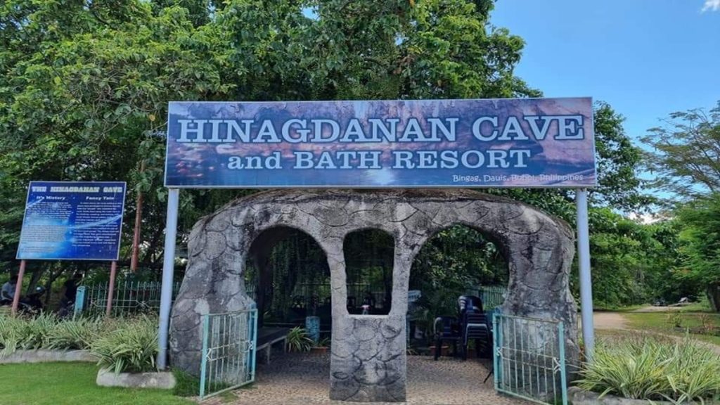 Sunlight entering Hinagdanan Cave through ceiling openings, illuminating limestone walls and a turquoise cave pool