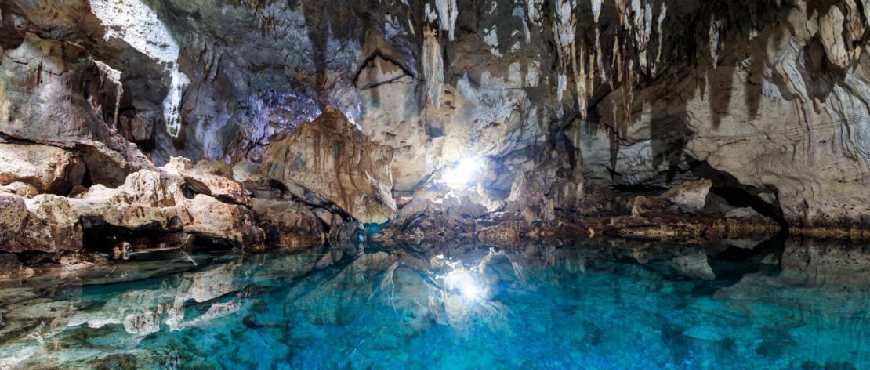 Interior view of Hinagdanan Cave in Bohol showing natural skylight, rock formations, and a clear underground lagoon