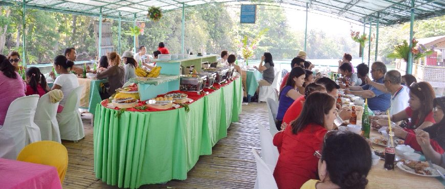 Passengers enjoying a buffet lunch on a covered Loboc River cruise boat with green table skirts and riverside jungle visible in the background.