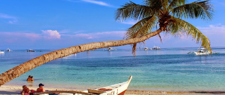 Bohol tour package featuring Panglao Island beach with turquoise water, palm trees, and traditional boats