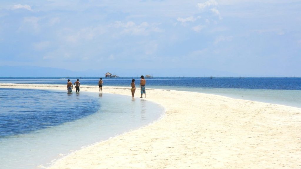 White sandbar at Virgin Island in Bohol with visitors walking along shallow turquoise water under a clear blue sky.